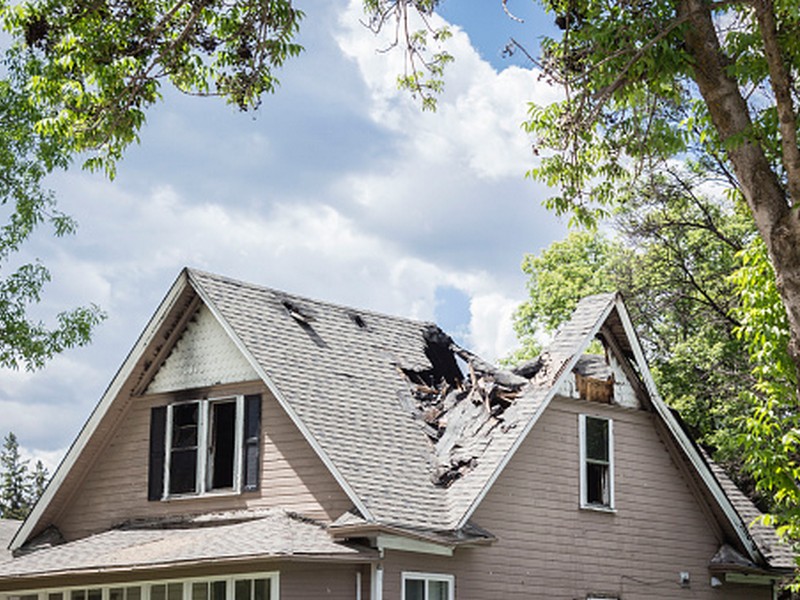 roof of a house that has burned and fallen in under blue sky with cloud in summer time.